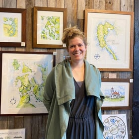 woman standing and smiling as featured artist with framed illustrations of maps