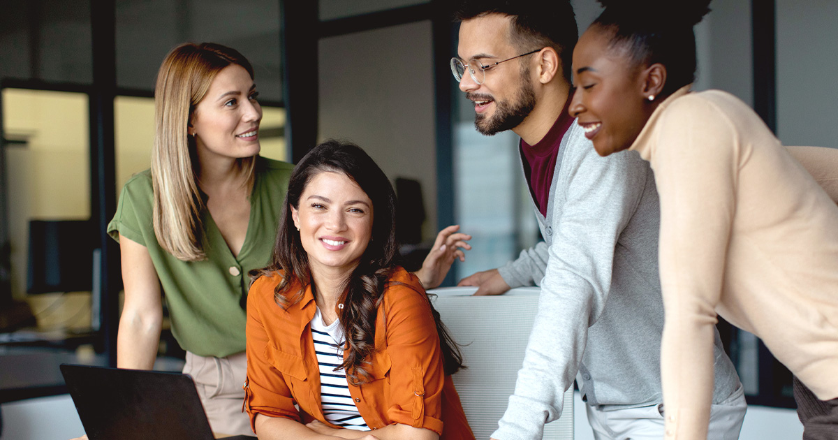 group of four people huddled at a desk with laptop in middle of discussions