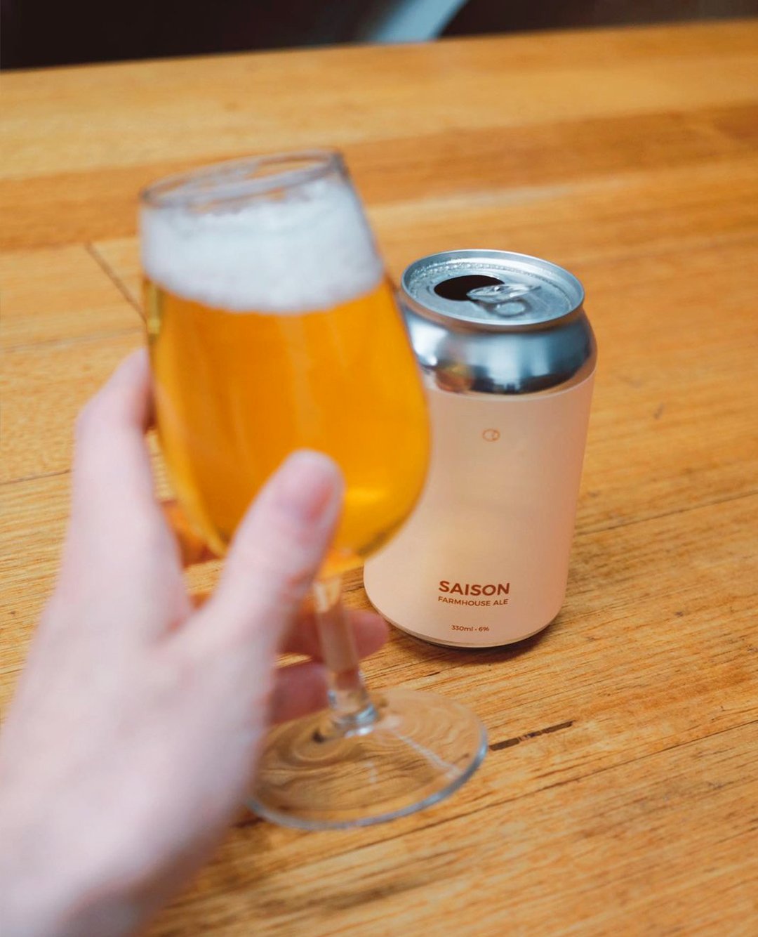 person holding a glass of saison farmhouse ale from a can