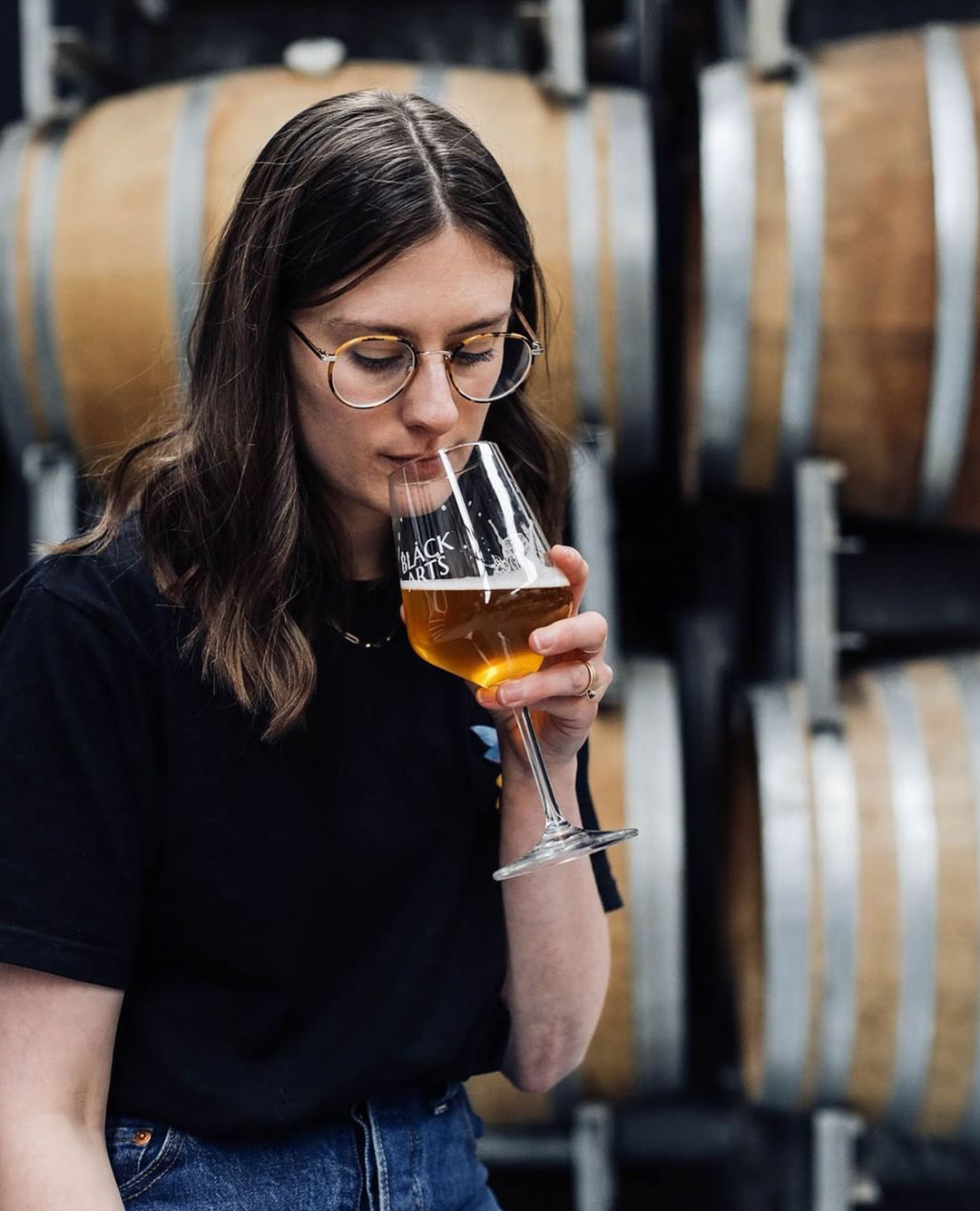 woman drinking beer from glass and barrels in the background