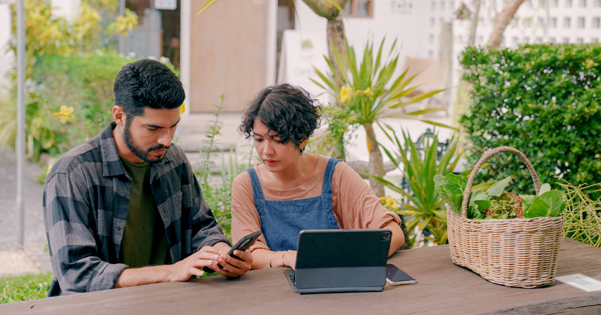 two people sitting outoors looking at devices on table