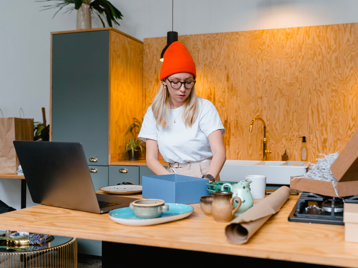 small business person preparing products to ship on kitchen counter laptop in front