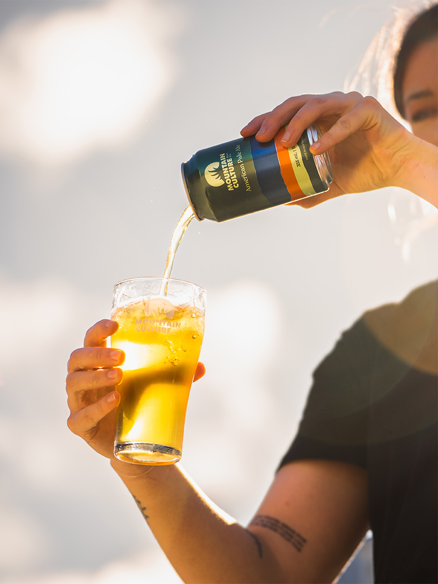 person holding glass pint pouring beer from can