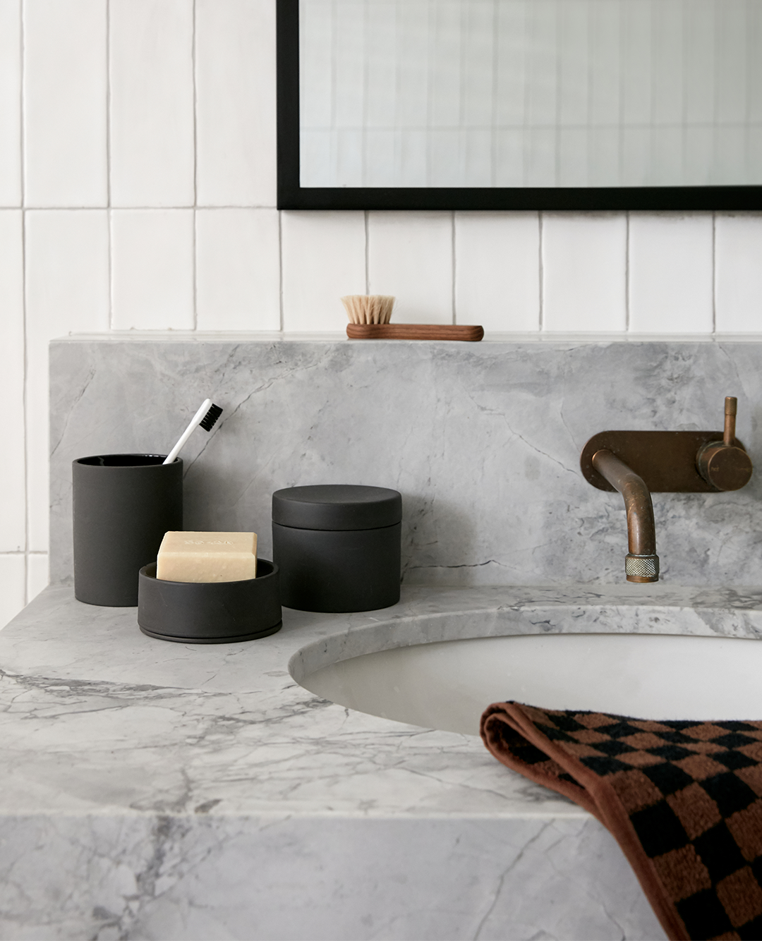 a checkered towel and containers for handsoap, toothbrush and hair brush on bathroom counter