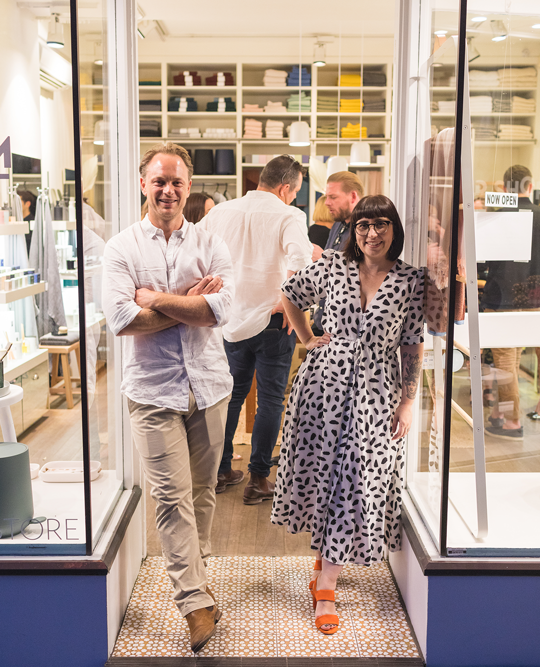 man and woman pausing outside of their store with a crowd of people inside