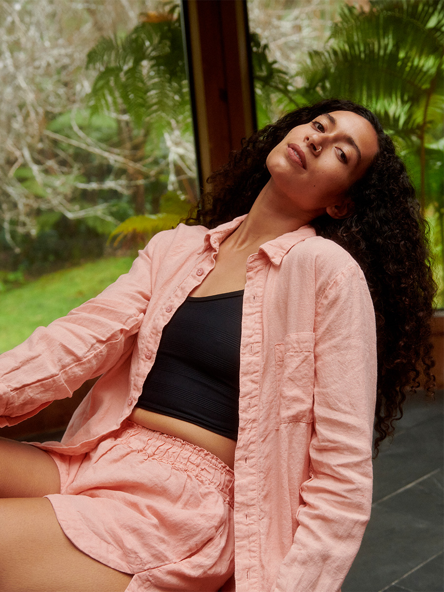 woman wearing pali swim linen tops and bottoms sitting down leaning backwards with garden in the background