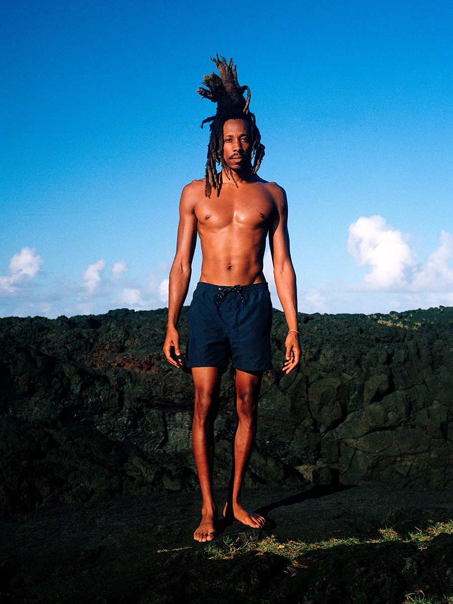 man wearing pali swim swimwear bottoms standing on rocky background skyline in the background