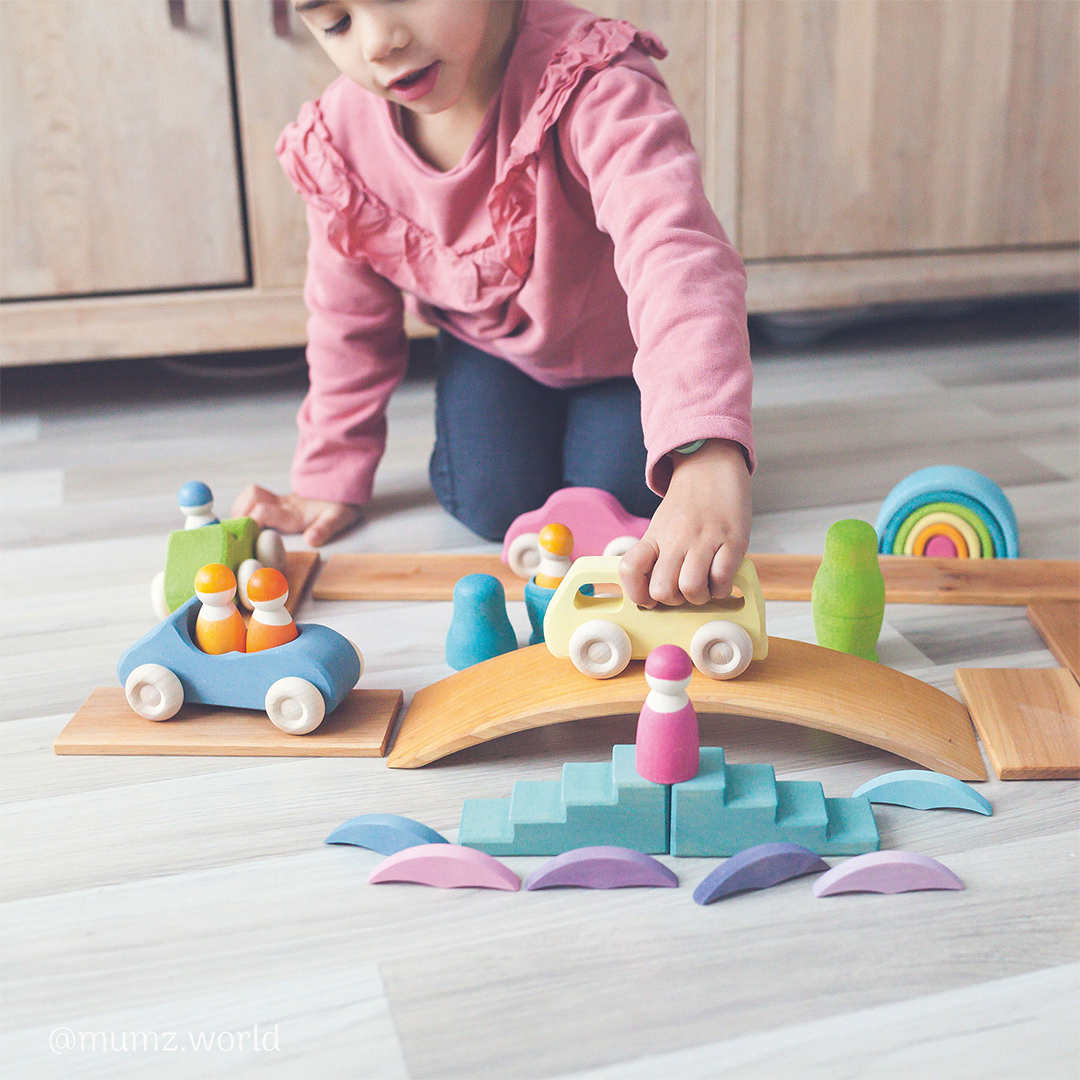 child playing with toy cars and bridges made of wood